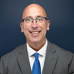 James Klein smiles into the camera against a dark blue background.